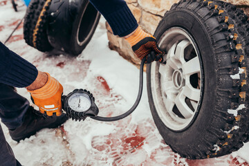 Close up mechanic inflating tire and checking air pressure with gauge pressure outdoors. Pilot preparing classic car before snow race during winter.