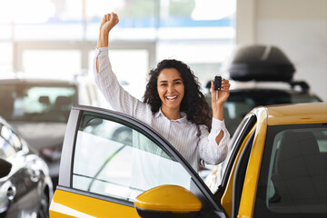Emotional brunette woman buying new car, showroom interior