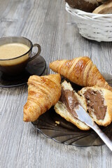 Croissants with chocolate cream and coffee on the rustic wooden background. Closeup