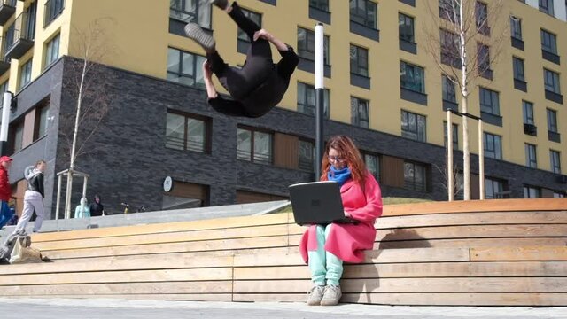 Caucasian man doing somersaults in the street and sits down next to the woman. The guy meets the girl in an unusual way.