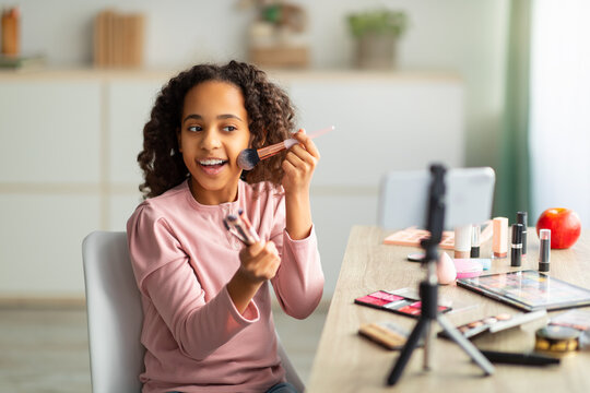 Beauty blogging. Cheerful african american teen recording cosmetics product review, using phone on tripod