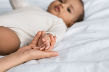 Cute little African American baby holding hands with mom