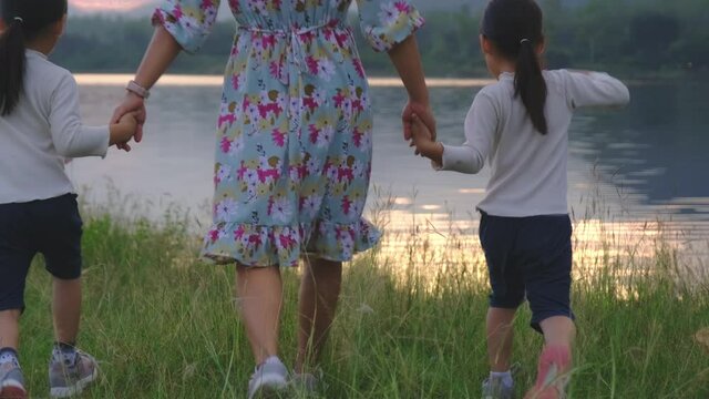 Happy mother and children walk hand in hand on a summer day by the lake at sunset. Happy family spent together on vacation.