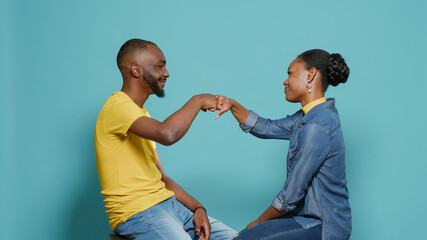 Obraz premium Couple sitting in studio and bumping fists together to show support and respect. Man and woman doing fist bump after deal and achievement, smiling at camera over isolated background.