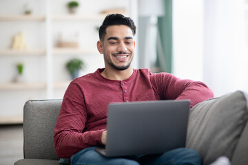 Positive arab guy surfing on social media, using laptop
