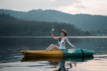 Kayaks in the lake. Tourists kayaking on mirror lake. taking photo when travel activity. woman playing in water in sunset. active woman rowing boat in lake with mountain view in evening.