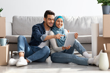 Happy muslim family sitting on floor with pad among boxes