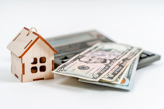 A wooden model of the house stands with a calculator and dollar bills on a white background. Business concept, real estate purchase