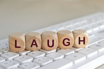 Wooden cube with the word  text.LAUGH on the keyboard Business concept.