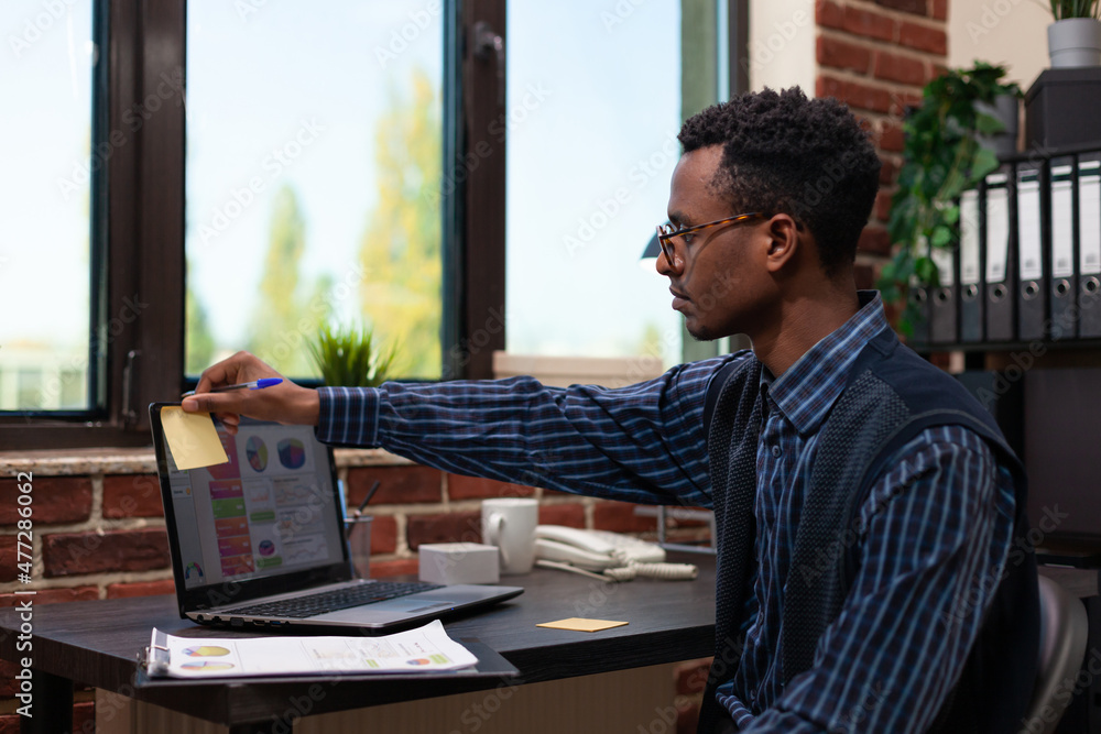 Poster startup employee sitting at desk sticking yellow post it on corner of laptop screen with business ch