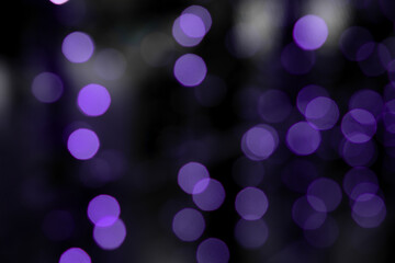 Defocused bokeh lights on black background, an abstract naturally blurred backdrop for Christmas eve or birthday party. Festive light texture. Violet blue garland in blur. Color 2022