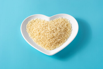 Raw rice on heart shaped plate on blue background