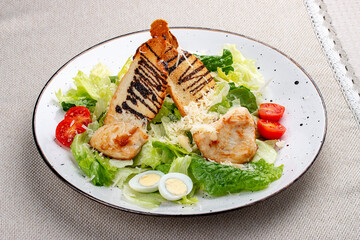 Caesar salad with chicken on a white decorative plate. A classic salad.