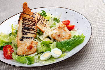 Caesar salad with chicken on a white decorative plate. A classic salad.