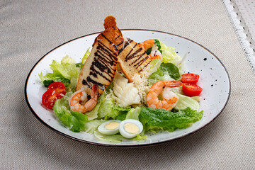 Caesar salad with shrimp on a white decorative plate. A classic salad.