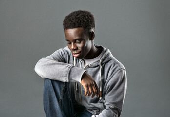 Confident African American male millennial sitting in gray studio and smiling