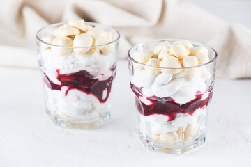 Dessert with aquafaba meringue, coconut cream and cherries in glasses on a light table.
