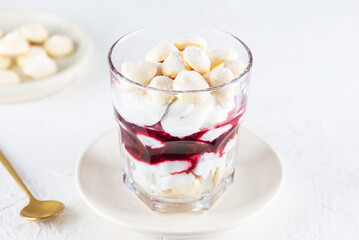 Dessert with aquafaba meringue, coconut cream and cherries in a glass on a light table. Sugar, lactose free, vegan.
