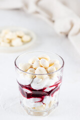 Sweet dessert with aquafaba meringue, coconut cream and cherry in a glass on the table. Sugar, lactose free, vegan.