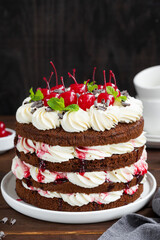 Naked Black forest cake, Schwarzwald pie. Cake with dark chocolate, whipped cream and cherry on a dark wooden background. Copy space.