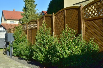 Moderner Holz-Sichtschutzzaun und Gehölzpflanzung um eine Hauseinfahrt als Grundstücksabgrenzung