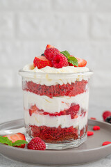 Red Velvet cake trifle with fresh berries in a glass jar on a gray concrete background. Dessert for Valentine's Day. Copy space.