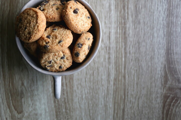 Ceramic bowl filled with chocolate chip cookies on wooden table. Flat lay.