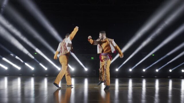 Handsome Caucasian men dancers performs traditional folk dance on a stage smoke, spotlight 4K. Armenian ensemble in traditional costume. Black background