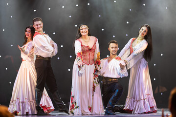 A collective of musicians, singers and dancers in gypsy costumes perform on stage.