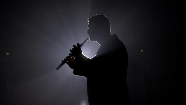 Person is playing the duduk, flute on black background 4K. Man playing classical music in the dark on a stage