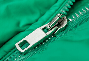 Fragment of a green jacket made of waterproof fabric with seams, metal button and opened zip...