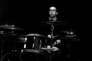 Young beraded man in glasses playing drums	