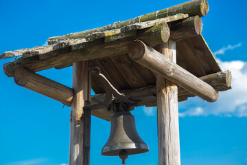 ancient bell under a wooden roof against the blue sky