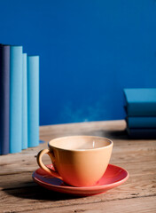 Fototapeta na wymiar Yellow cup of coffee or tea with hot steam, on table wooden with light blue books and blue background.