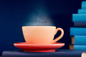 Yellow cup of coffee or tea with hot steam, on book with light blue books and blue background.
