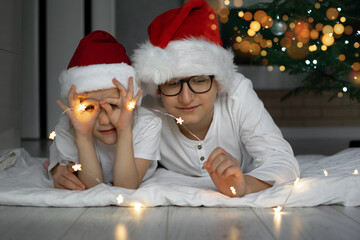 Fototapeta premium a boy in a Santa Claus hat and glasses lies on the floor and smiles