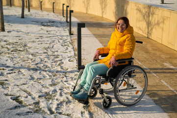 Obraz premium Caucasian woman with disabilities rides on a chair in the park in winter. Girl on a walk in a wheelchair. 