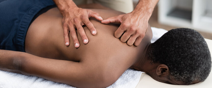 chiropractor doing back massage to african american patient in clinic, banner