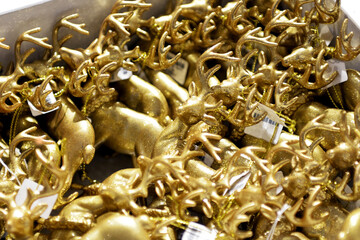 A lot of shiny, golden deer in the form of Christmas tree decorations lying in a box in a store, close-up, selective focus.