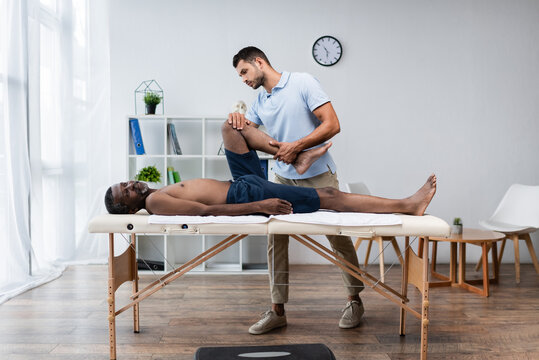 full length view of rehabilitologist treating african american man on massage table