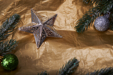 Christmas composition on a gold crumpled paper background. Silver star with fir balls and fir branches, top view.
