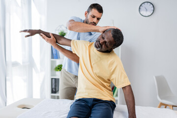 rehabilitologist stretching arm and neck of african american man in clinic