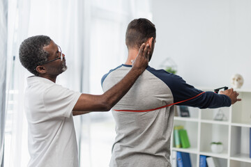 Obraz premium african american rehabilitation trainer assisting man working out with resistance band