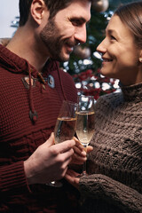 Young couple clinking glasses next to a beautiful decorated Christmas tree