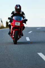 Red motorcycle with driver in leather suit while driving on a road with a slight side position, photographed from the front..