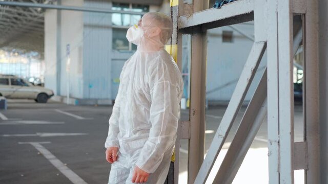 Despair healthcare worker in white covid protective overalls. Tired Male caucasian doctor grabs his head cower in depression during coronavirus pandemic. Paramedic overworked tired and angry