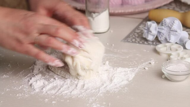 A woman makes confectionery mastic from powdered sugar. Kneads it with his hands. Close-up.