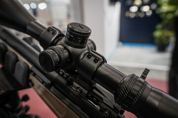 Black shooting scope optics mounted on rifle displayed at weapons exhibition fair, closeup detail...