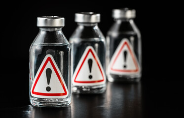 Three vaccine bottles with red triangle exclamation mark sign on label, black background