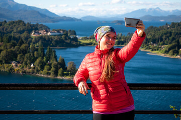Mujer tomando una selfie en mirador  del circuito chico de la ciudad de Bariloche. Patagonia Argentina - obrazy, fototapety, plakaty